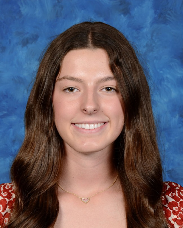 high school student with long brown hair smiles wearing a heart necklace
